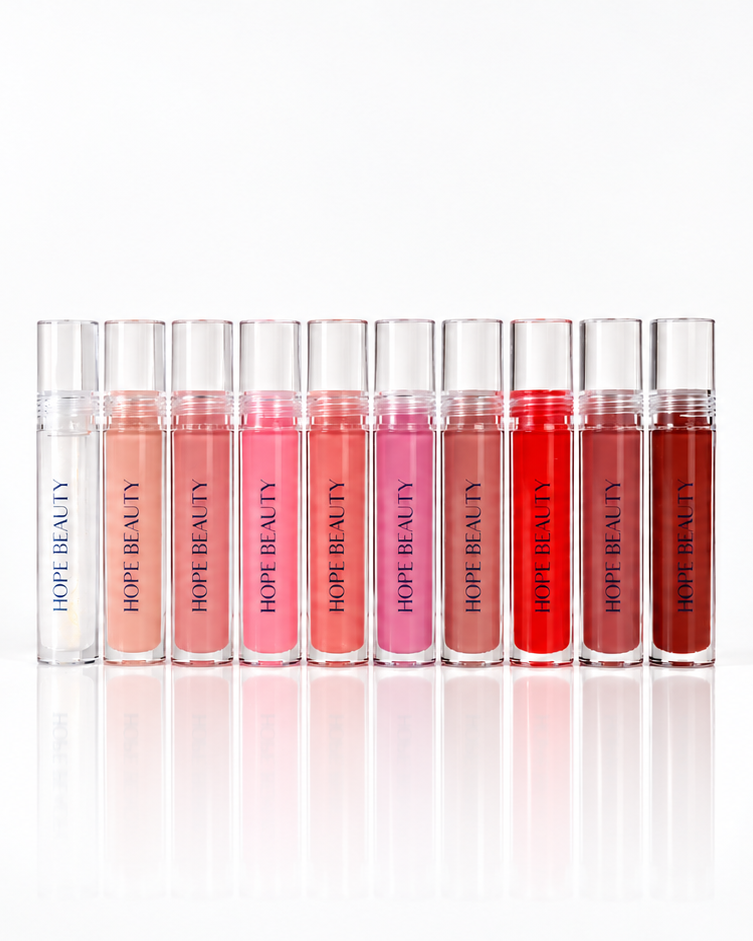 A row of ten clear lip gloss tubes with silver caps, displaying a gradient of lip colors from pale pink to deep red, on a clean white background with a soft reflection below. Christian makeup. Faith based makeup. Makeup inspired by women of the bible. Hope Beauty Lip Reflect.